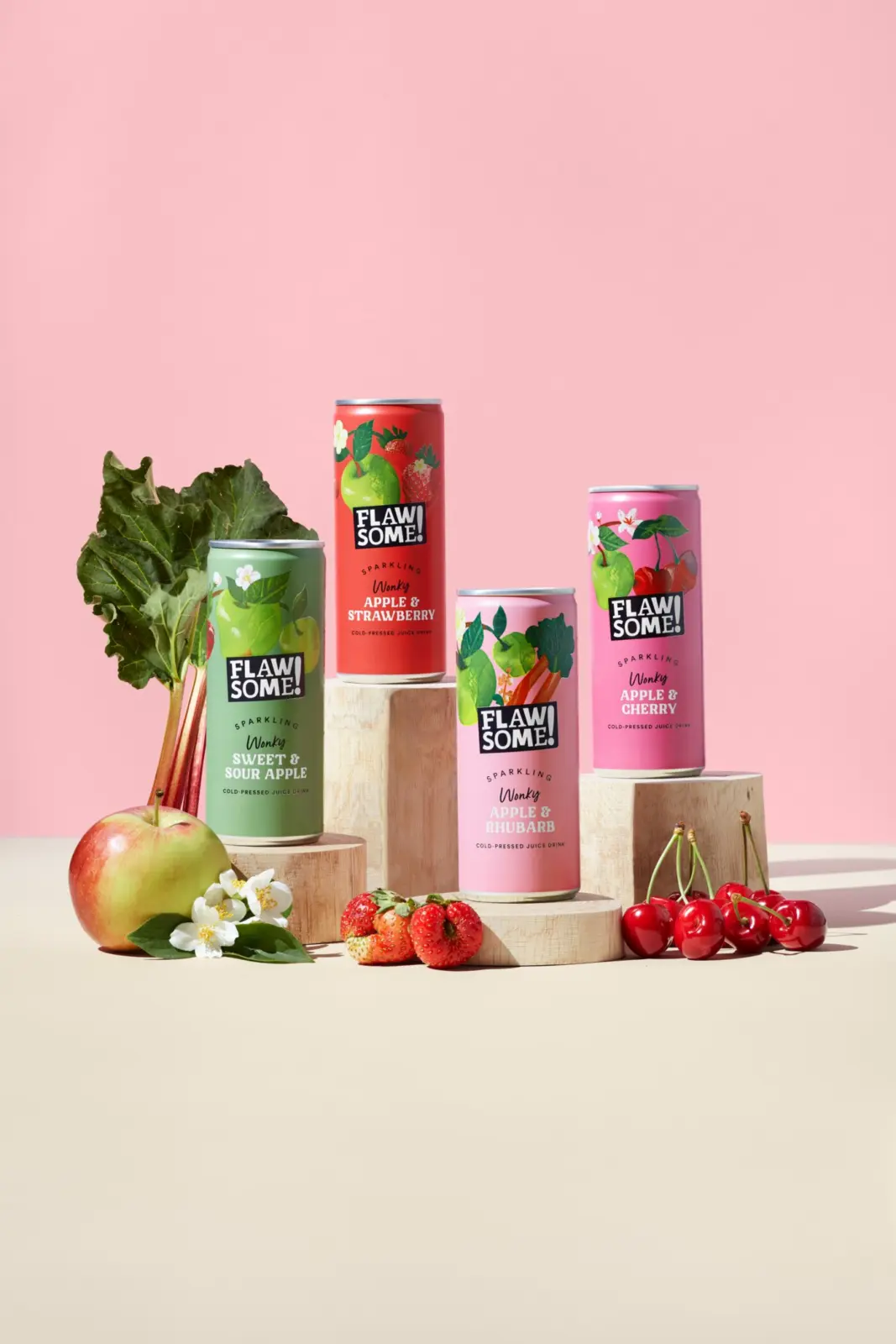Four Flawsome Drinks sparkling cans on wooden plinths with fresh fruit beside them