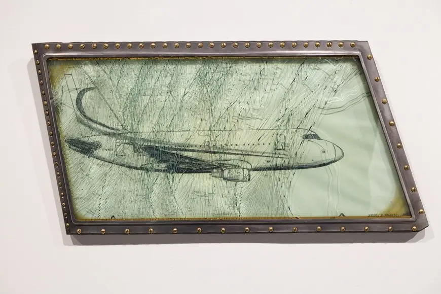 A drawing of an aeroplane set behind cracked glass in a studded metal frame by Vahakn Arslanian.