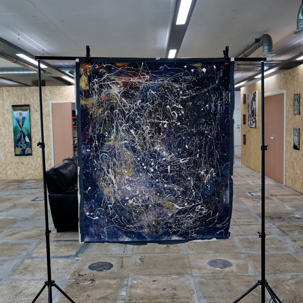A large dark abstract canvas hanging on a stand in the studio