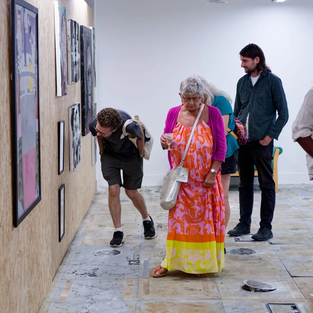 Guests in bright summer clothes talking beneath the hung artwork
