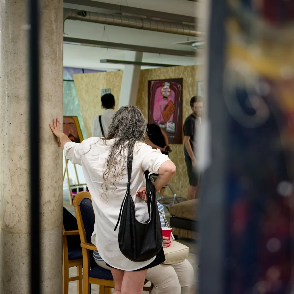 A visitor with long grey hair studying work on the studio wall
