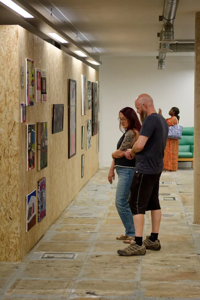 Visitors walking the long corridor of framed works at Arclite House