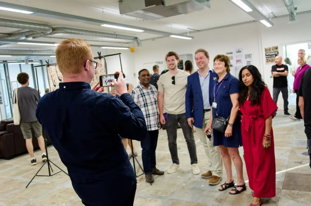 A guest photographing a group of visitors on a phone during the opening
