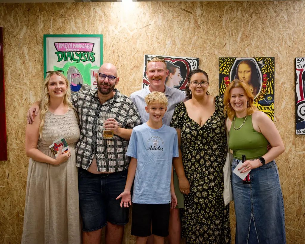 A family group of six posed in front of the artwork
