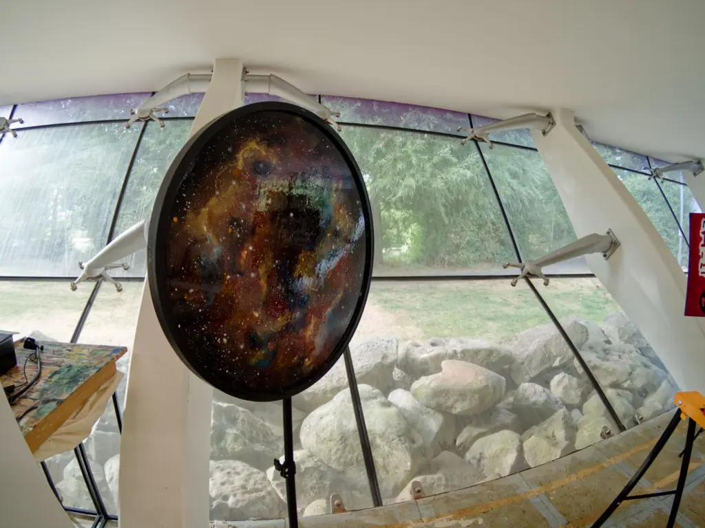 A dark circular artwork hanging in the glass-walled studio