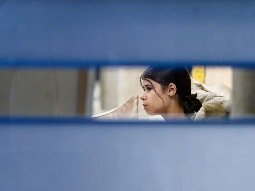 A guest seen through the studio window blinds