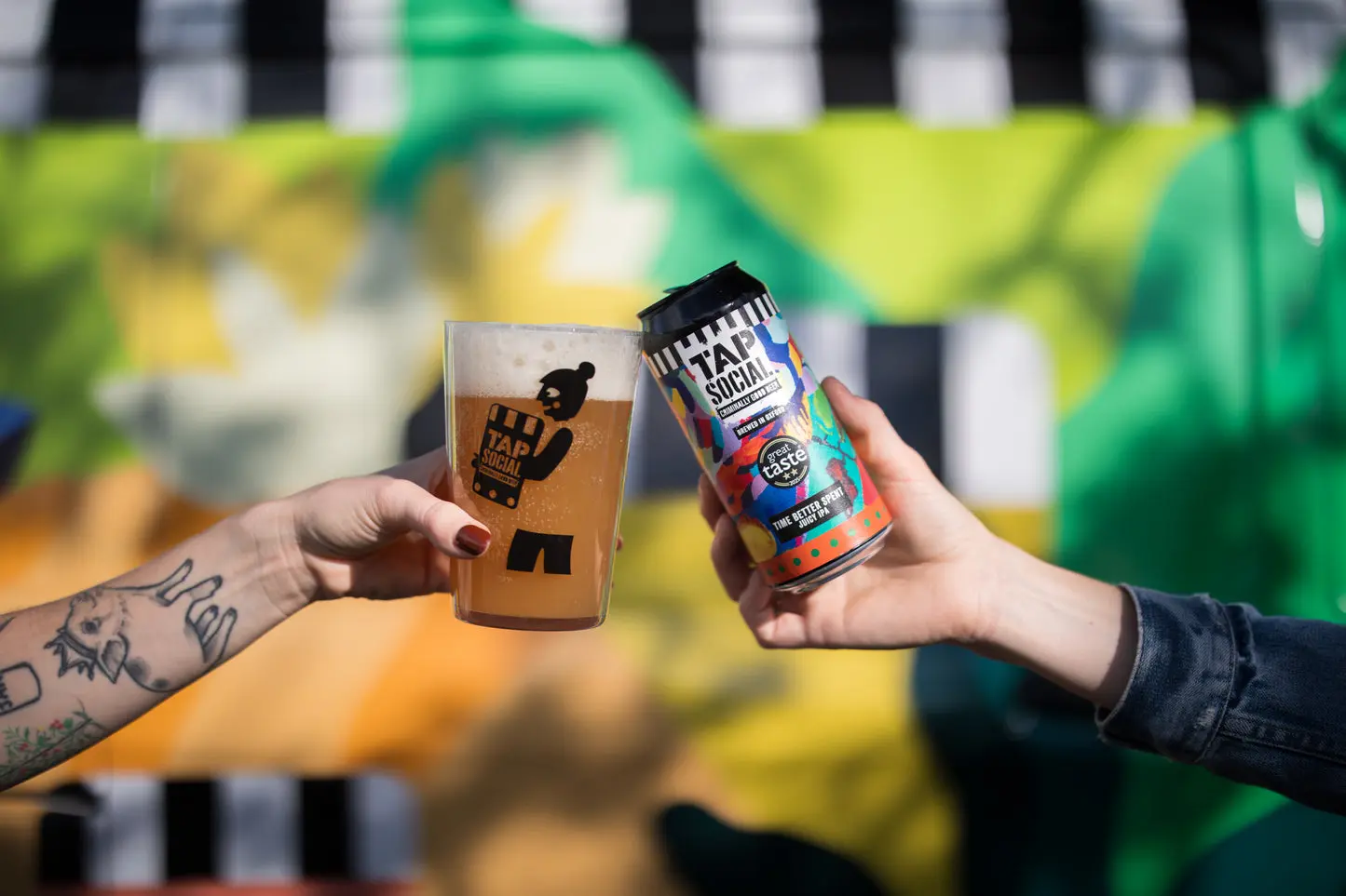 Two people toasting with a glass and a can of Tap Social Movement Time Better Spent juicy IPA